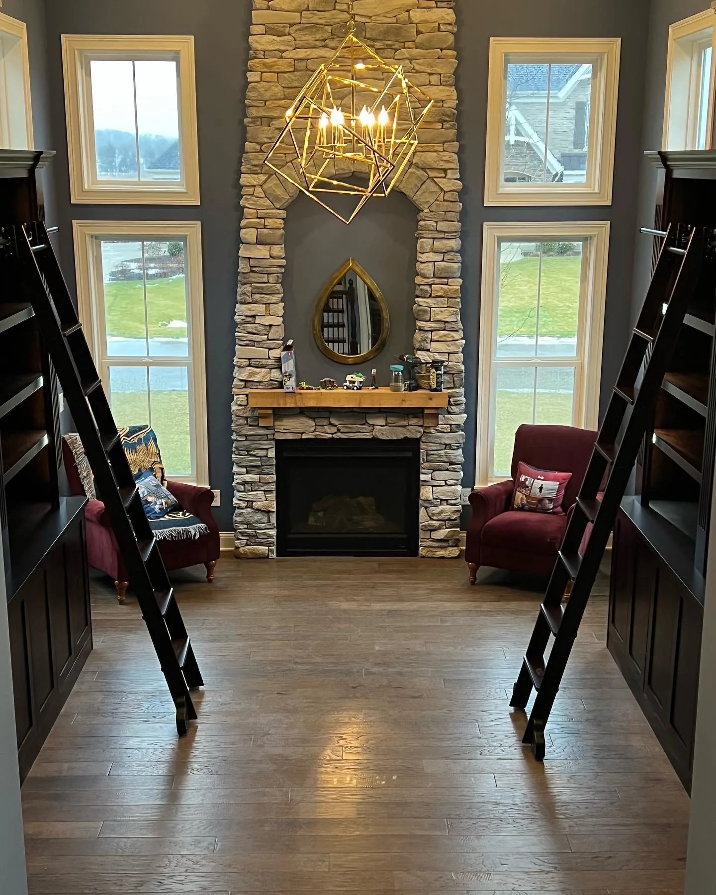 A two-story built-in library wall with rolling ladders, flanking a stone fireplace